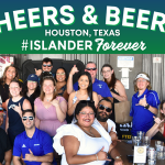 Group of Texas A&M University-Corpus Christi alumni posing together and smiling at a "Cheers & Beers" alumni mixer event in Houston, Texas. The group includes individuals of various ages and some are holding drinks. "Islander Alumni Association" and "#ISLANDERForever" are prominent in the design.